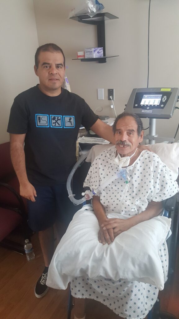 A man standing next to an older man in hospital.