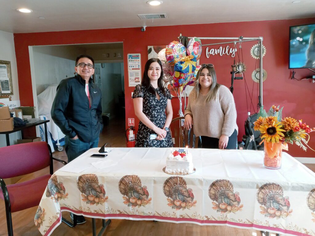 Three people standing in front of a table with a cake on it.
